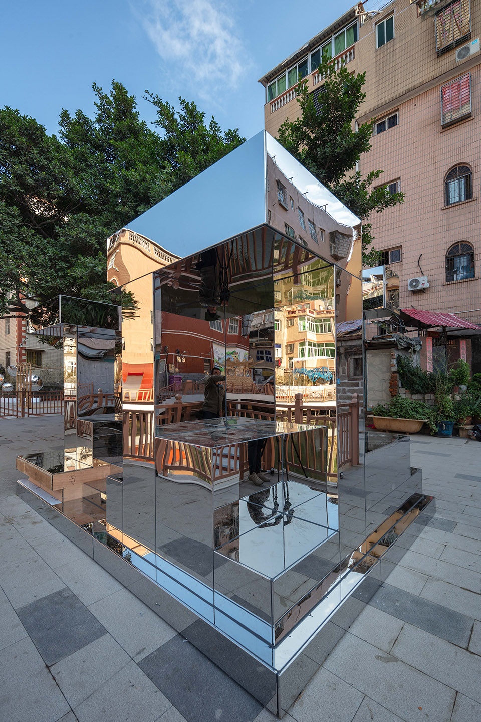 Tall mirror-polished stainless steel column and stepped base reflecting surrounding houses, Sea Reef installation in Xiamen