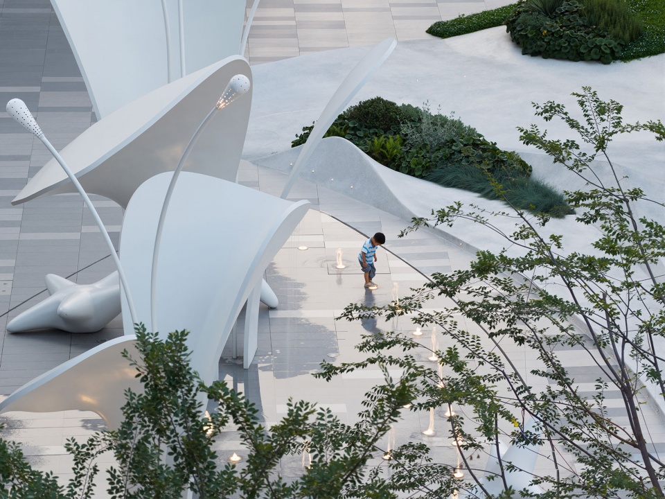 White freeform sculptural canopies and light poles beside a fountain plaza with a child walking through, Splash Plaza Yichang